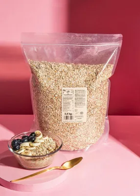 A large bag of oats is shown behind a bowl of oatmeal topped with blueberries and banana slices, with a golden spoon in the foreground.