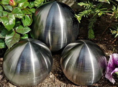 Three metallic spheres are placed on the ground among plants and flowers.