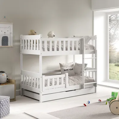 A white wooden bunk bed with a pull-out drawer, set up in a child's room with toys and a window view.