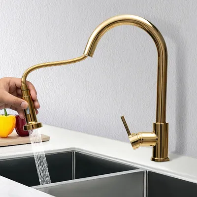 A gold faucet is shown in use, with water running into a sink. There are also some vegetables in the background.