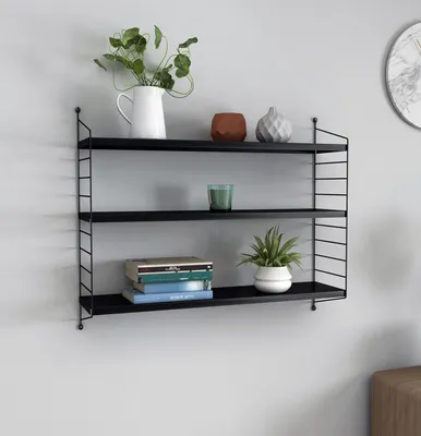 A black metal wall shelf with three shelves, decorated with plants, books, and decorative objects.