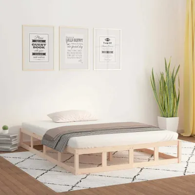 A wooden bed frame with a mattress and bedding in a room with framed pictures on the wall and a plant.