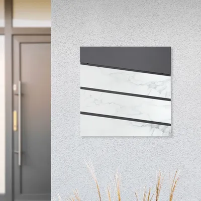A mailbox with a newspaper compartment mounted on a textured wall next to a door.