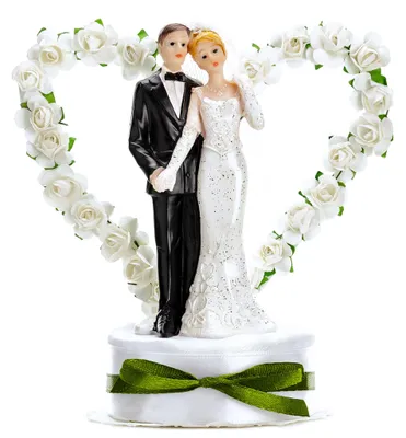 Tortenaufsatz Hochzeitspaar in Weiß mit Herz aus Rosen, Braut im Kleid und Bräutigam im Anzug auf dekorativem Sockel mit grünem Band.