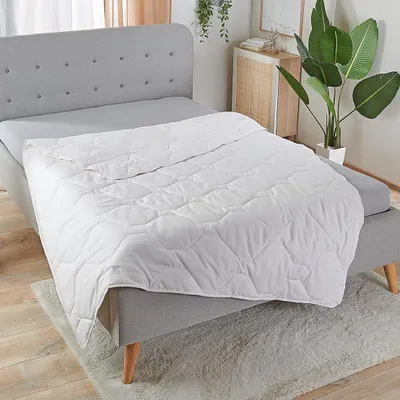 A white quilted blanket is laid out on a bed with a grey headboard and grey fitted sheet.