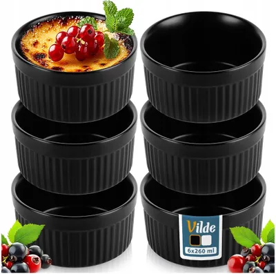 A set of black ceramic ramekins, one filled with a crème brûlée and garnished with berries and mint.