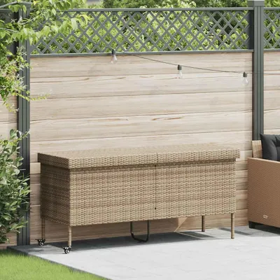 A beige poly rattan garden storage box with wheels is placed on a patio in front of a wooden fence with string lights.