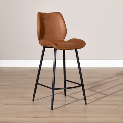 A single brown leather bar stool with black metal legs is shown against a light gray wall and a light wood floor.