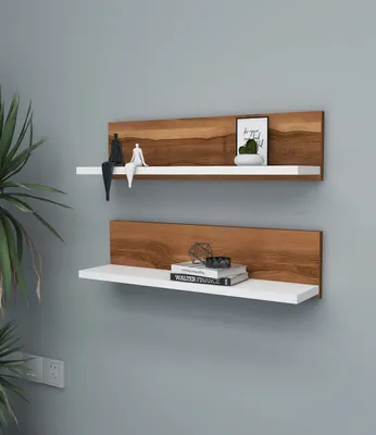 Two white shelves with a walnut wood backing are mounted on a light gray wall. The top shelf holds two small figurines, a framed picture of a cactus, and a small white object. The bottom shelf displays two books and a geometric sculpture.