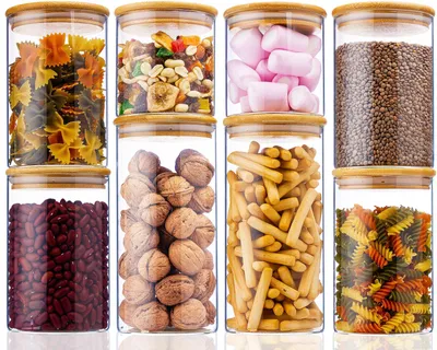 Acht klare Glas-Vorratsgläser mit Bambusdeckeln, gefüllt mit verschiedenen Trockenwaren wie Nudeln, Nüssen, Marshmallows, Linsen und Bohnen