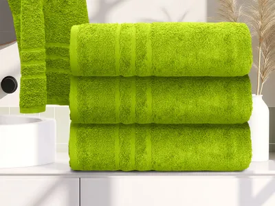 Three green towels are stacked on a white surface, with a sink and decorative reeds in the background.