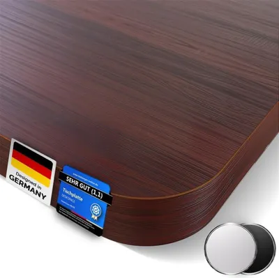 A close-up, angled view of a dark brown wooden desk surface with rounded edges, featuring two small labels attached to the corner. Two circular metallic objects are in the bottom right corner.