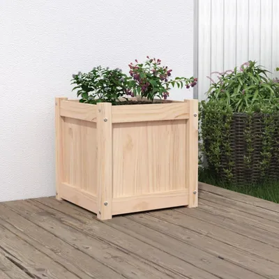 A wooden planter box with plants on a wooden deck next to a white wall.