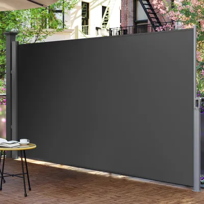 A dark gray retractable side awning is extended on a wooden deck, providing privacy. A small table with a book and cup is visible to the left.