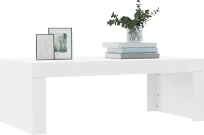 A white coffee table with two framed pictures and a vase of greenery on top.
