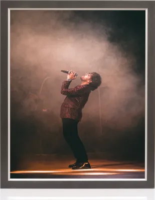 A man singing into a microphone on a stage with smoke and spotlights.