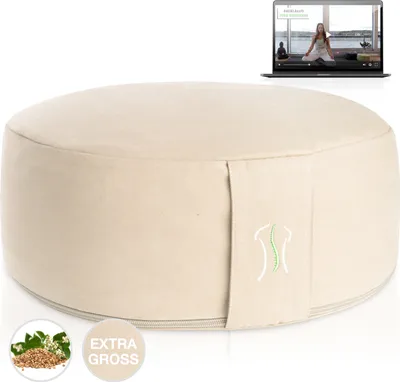 A beige meditation cushion with a laptop displaying a yoga video in the background.