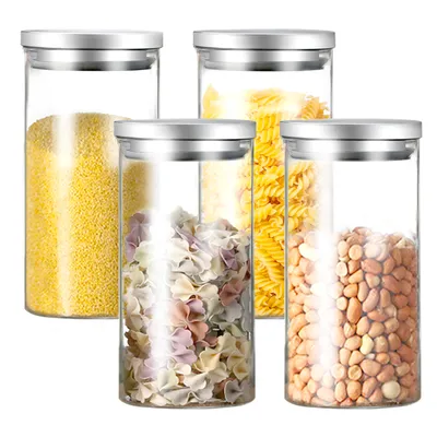 Four glass storage jars with silver lids are arranged in a group on a white background. The jars contain different food items: one with yellow grains, one with colorful pasta shapes, one with spiral pasta, and one with peanuts.