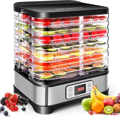 A food dehydrator filled with various fruits and vegetables, placed on a surface with a pile of fresh berries and bananas nearby.