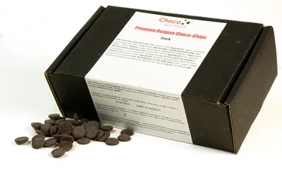 A black box of chocolate chips with some chips spilled in front of it.