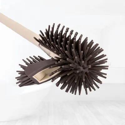 A toilet brush with brown silicone bristles and a beige handle is shown in a bathroom setting, resting against a white toilet bowl.