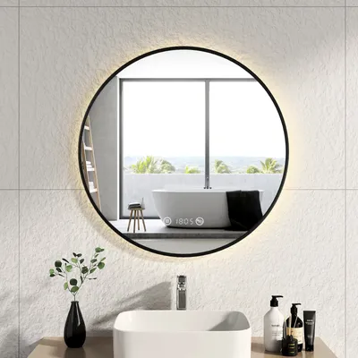 A modern bathroom with a sink, faucet, and a round LED mirror reflecting a bathtub and a window.