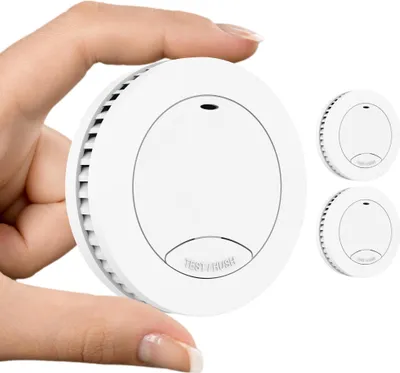 A hand holding a smoke detector with two other smoke detectors in the background.