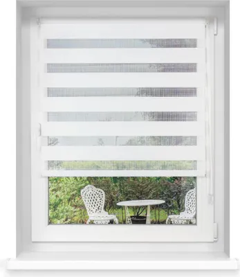 A white window with a white roller blind partially covering the view of a garden with two white chairs and a small table.