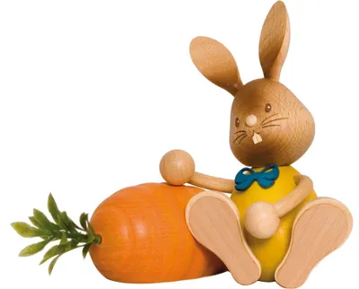 A wooden bunny figurine sitting next to a wooden carrot.