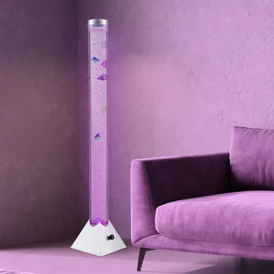 A tall, clear bubble lamp with purple water and decorative fish is placed next to a plush purple sofa in a room with purple walls.