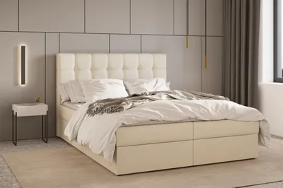 A bedroom scene featuring a beige upholstered bed with a tufted headboard, white bedding, and a bedside table with a lamp.