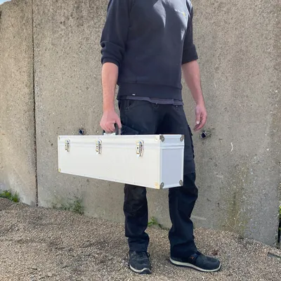 A person is holding a silver case in front of a concrete wall.