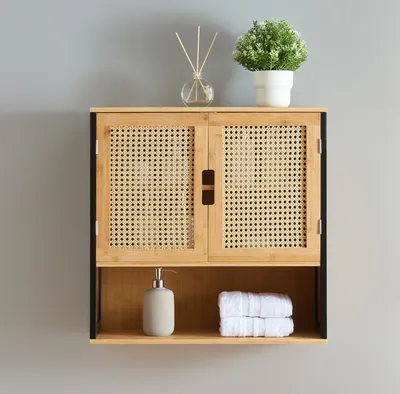 A wall-mounted cabinet with woven doors, a shelf below, and decorative items on top.