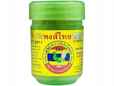 A green jar of herbal balm with Thai writing and a picture of a bird.