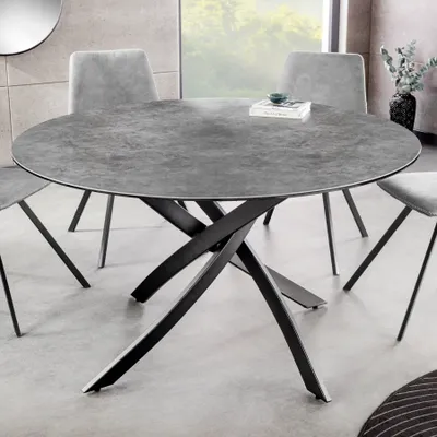 A round dining table with a ceramic top and black metal legs, surrounded by chairs in a modern dining room setting.