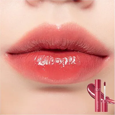 A close-up of lips with glossy pink lipstick, with a product bottle and applicator in the bottom right corner.