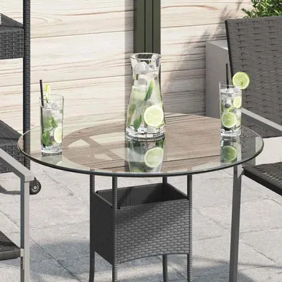 A round glass tabletop with a wicker planter underneath, set on an outdoor patio with drinks on the table.