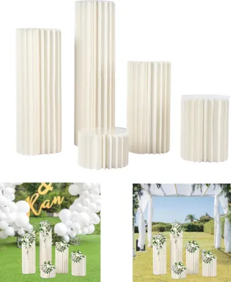A collection of white, fluted cylindrical pedestals of varying heights, displayed against a white background. Below this, two lifestyle shots show the pedestals used as decorative elements in event settings, one with balloons and signage, the other with fl