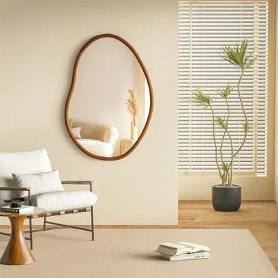 A modern living room scene with a mirror, chair, plant, and books.