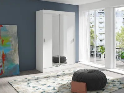A modern bedroom with a white sliding door wardrobe, a colorful abstract painting, and a round pouf on a patterned rug.
