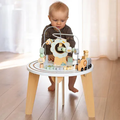 A baby is playing with a wooden activity table with a magnetic train and bead maze.
