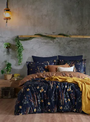 A bedroom scene with a bed dressed in dark blue bedding with a floral pattern, a brown duvet cover, and a yellow throw blanket.