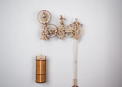 A wooden mechanical clock with gears and a pendulum hanging on a light gray wall.