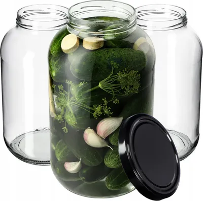 Three empty glass jars and one jar filled with pickles, dill, and garlic, with a black lid next to it.