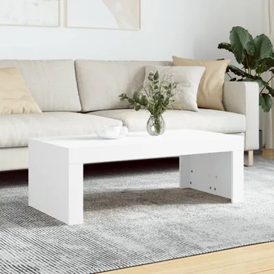A white coffee table is placed on a rug in front of a sofa. There is a vase with greenery on the table.
