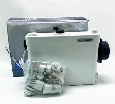 A white SaniPack-WC-Förderanlage sits on a white surface next to its packaging and a bag of accessories.