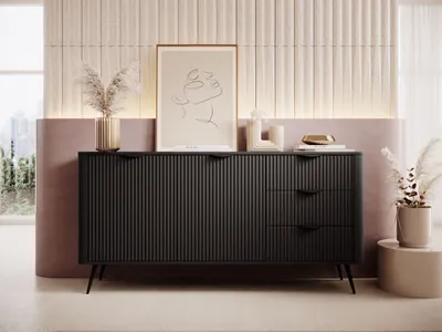 A black sideboard with fluted doors and drawers is displayed in a modern living room setting, decorated with dried pampas grass and a framed abstract line drawing.