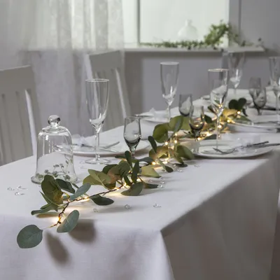 A table setting with a eucalyptus garland and fairy lights.