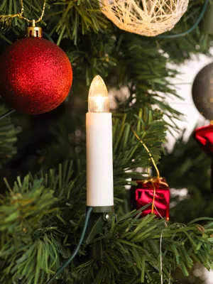 A close-up of a Christmas tree with decorations, including a lit candle-shaped LED light.