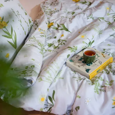 A cozy bed with floral bedding, a book, and a cup of tea.